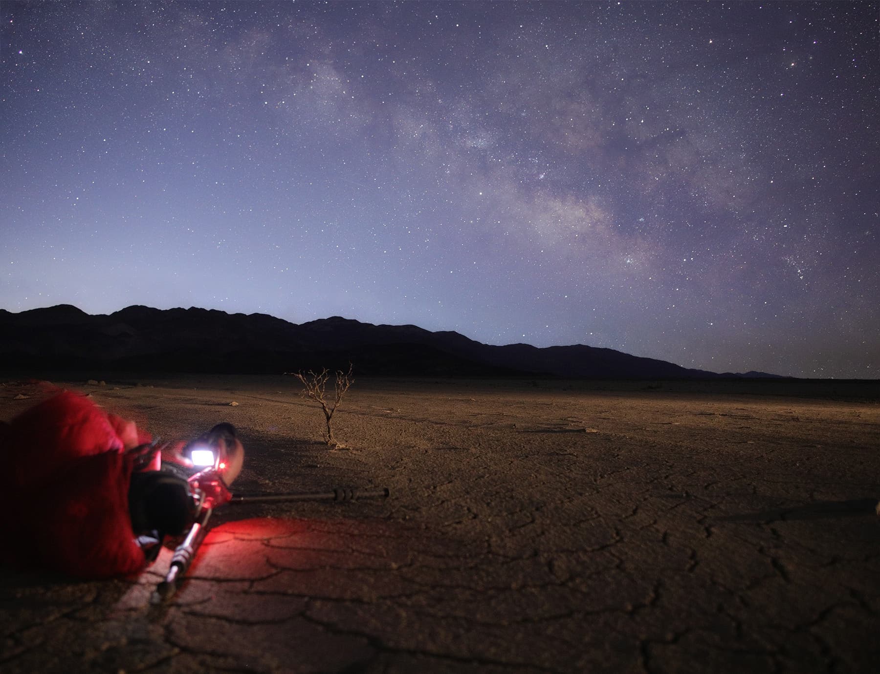 Photographer working cracked foregrounds under the Milky Way in Death Valley